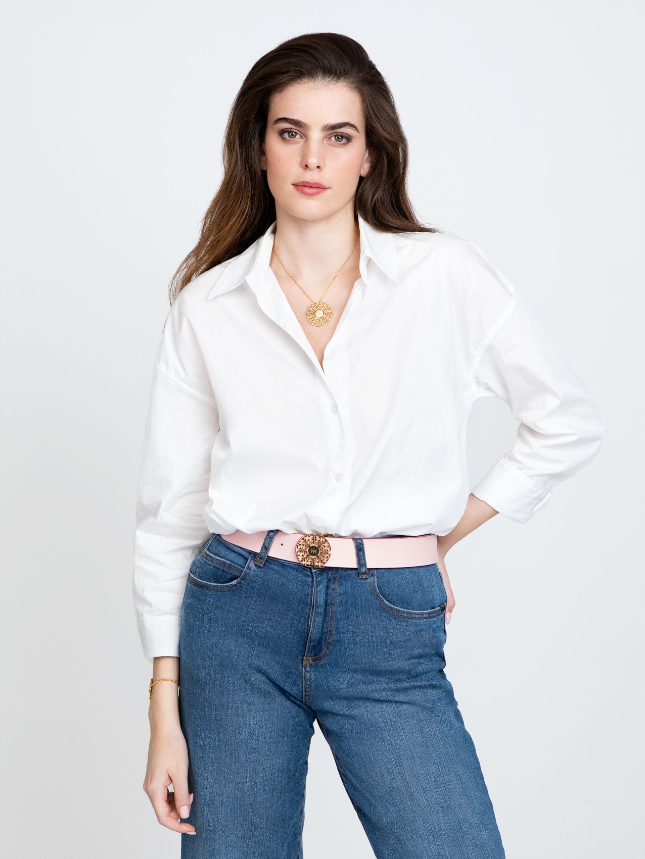 Dark Haired Woman in white shirt and jeans with pink belt and golden necklace