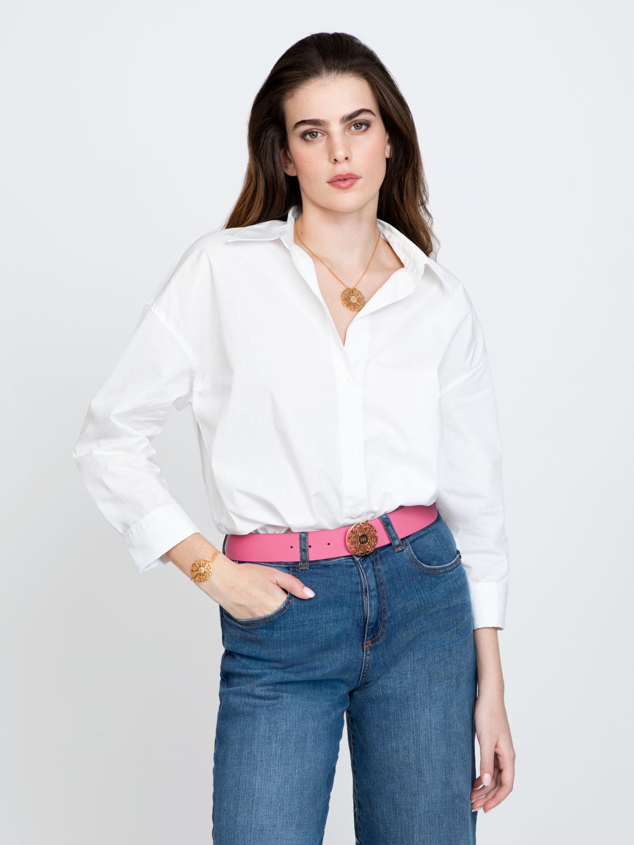 Dark Haired Woman in white shirt and jeans with pink belt and golden necklace