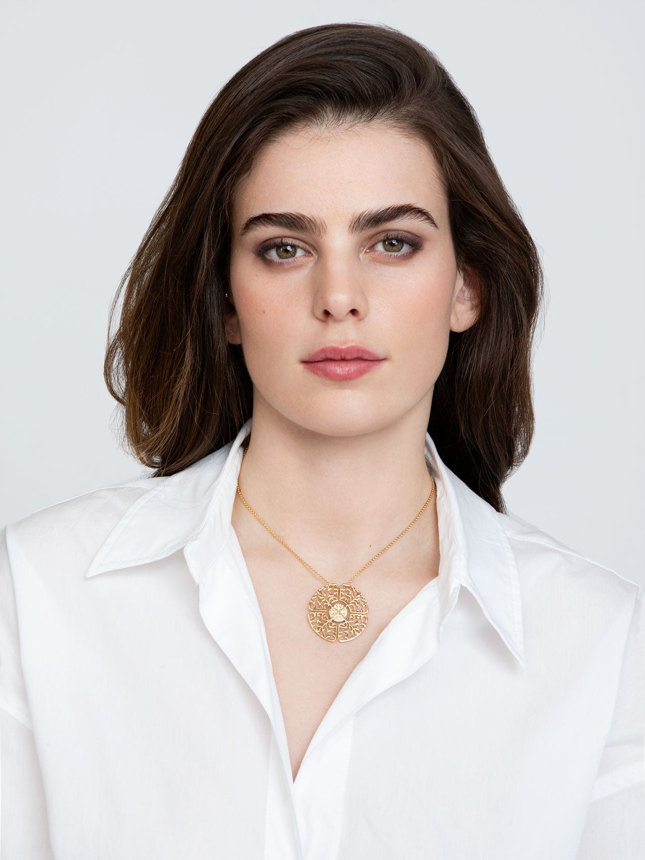 A young woman with black hair in white shirt wearing Big necklace gold plated statement medallion 